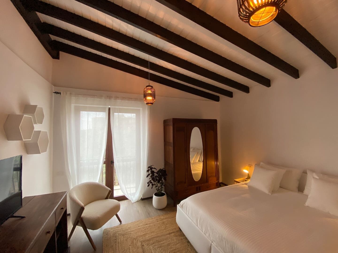 A bedroom with a bed, a desk, a chair, a wardrobe, and a hanging light fixture.