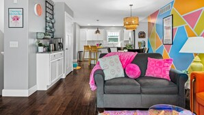 A modern living room with a grey sofa, colorful pillows, and a vibrant geometric wall design.