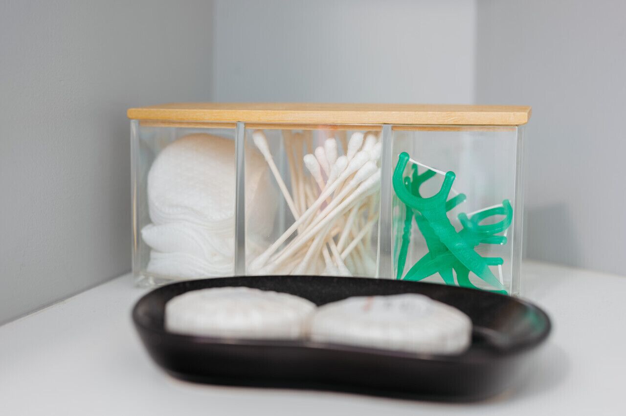 A storage unit with compartments containing cotton swabs, cotton buds, and a green plastic item.