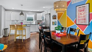 A modern kitchen with white cabinets, a wooden dining table, and a colorful geometric wall design.