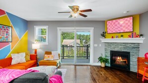 A living room with a fireplace, a ceiling fan, and a large window.