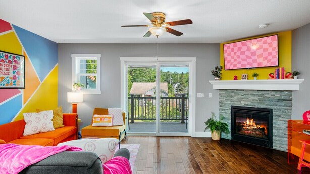 A living room with a fireplace, a ceiling fan, and a large window. - The Emerald Nest 3BR Townhome Near Downtown Beach Wineries (Traverse City)