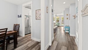 A modern kitchen with stainless steel appliances, a dining area with a wooden table and chairs, and a hallway leading to a living room with a blue table and a green couch. - Sandy Palms ~ Pet-Friendly Coastal Retreat with Golf Cart & Game Loft (Panama City Beach)