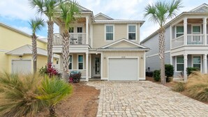 A two-story house with a front garage, a covered porch, and a paved driveway. - Sandy Palms ~ Pet-Friendly Coastal Retreat with Golf Cart & Game Loft (Panama City Beach)