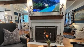 Una sala de estar con chimenea, un televisor montado encima y un rincón de descanso acogedor con sofá y sillones.