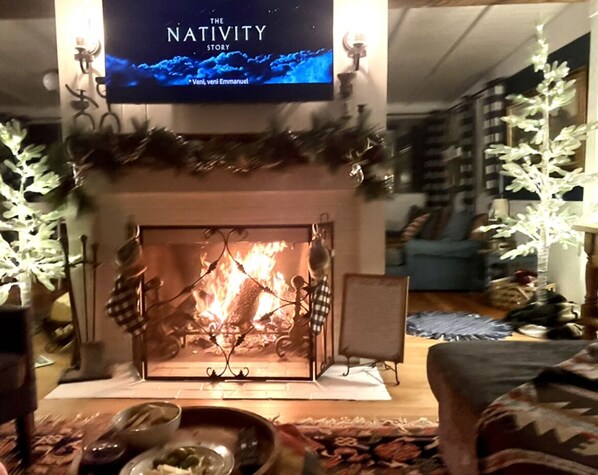 Un salon chaleureux avec une cheminée, un téléviseur fixé au-dessus et un sapin de Noël.