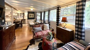Una habitación acogedora con techo de madera, un sofá con cojines estampados, una mesa de comedor y una ventana con cortinas a cuadros.