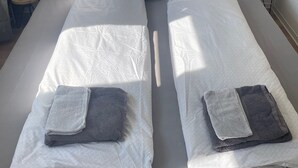 A double bed with white linens, two pillows, and two folded towels.
