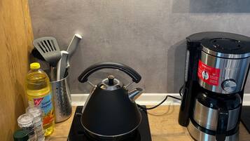 Una cocina con estufa, cafetera y diversos utensilios de cocina.