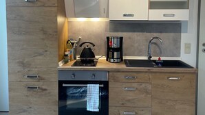 A modern kitchen with wooden cabinets, a built-in oven, a kettle, and a coffee maker.
