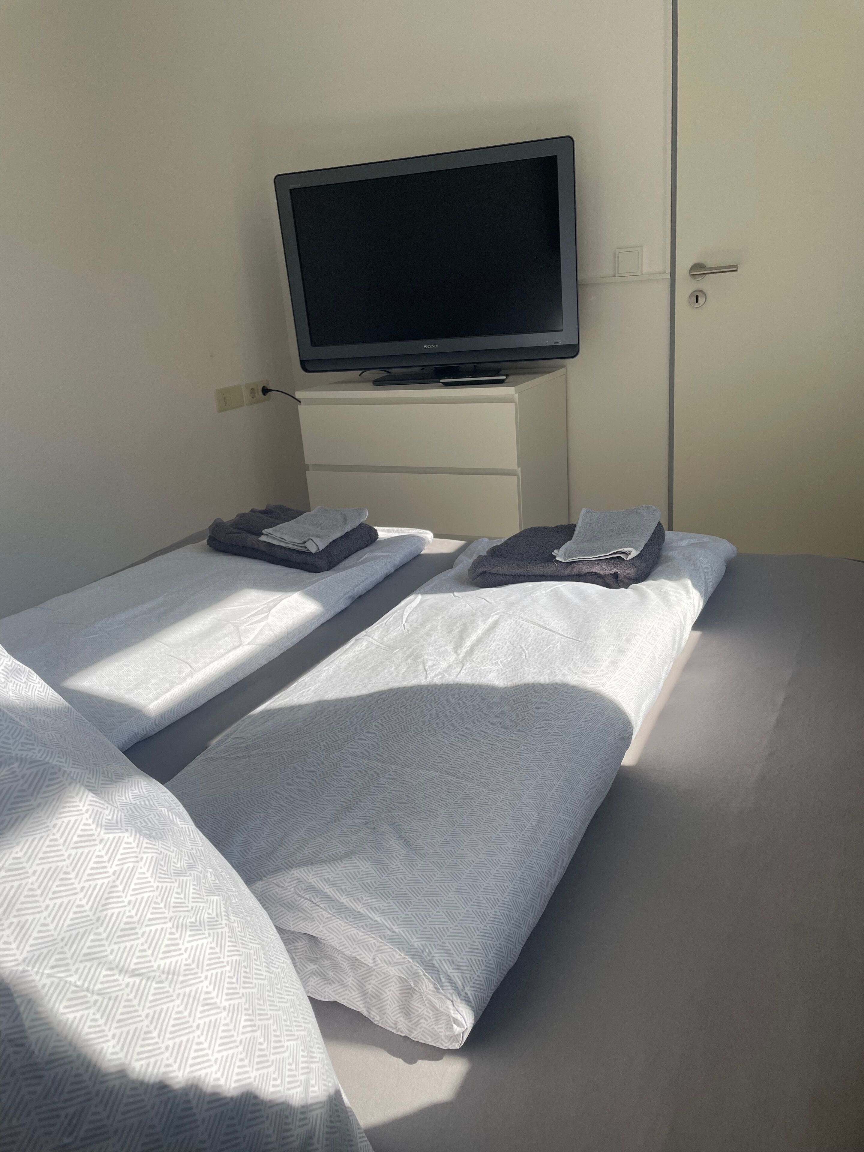 Una habitación de hotel con una cama, un televisor sobre un tocador blanco y una puerta.