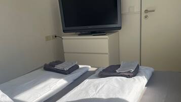Una habitación de hotel con una cama, un televisor sobre un tocador blanco y una puerta.