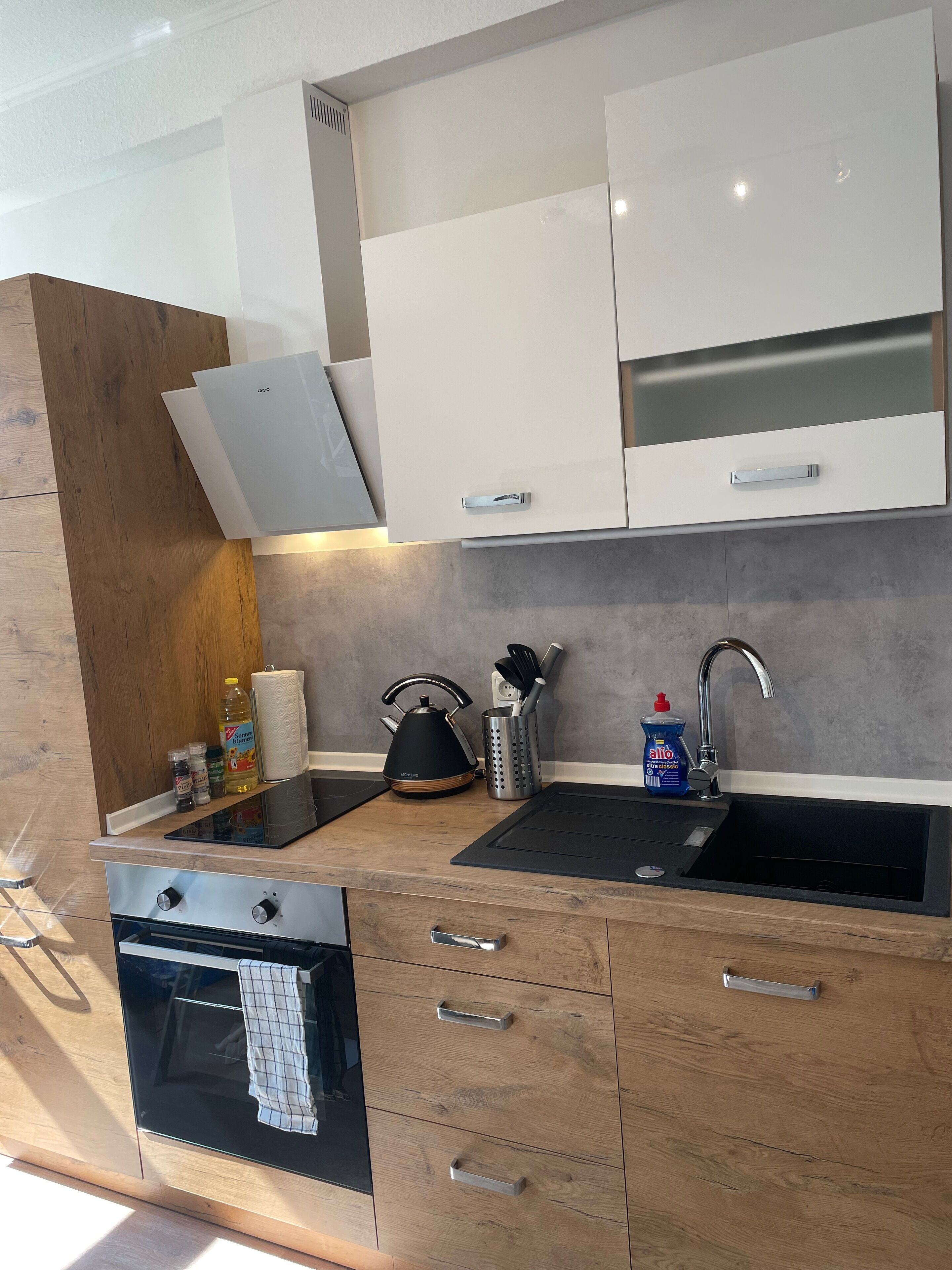 Eine moderne Küche mit einem schwarzen Spülbecken, Edelstahlgeräten, Holzschränken und einem eingebauten Backofen.