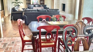 A spacious living area with a black leather sofa, a dining table with red chairs, and a stone fireplace. - Secluded Whoop Acre Ranch SLEEPS 25-LOADED with entertainment (Bryan)