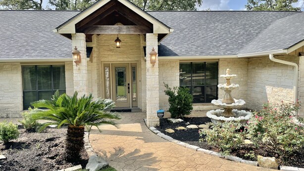 A two-story house with a stone facade, a front porch, and a landscaped garden with a fountain. - Secluded Whoop Acre Ranch SLEEPS 25-LOADED with entertainment (Bryan)