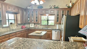 A kitchen with granite countertops, wooden cabinets, a dishwasher, and a refrigerator. - Secluded Whoop Acre Ranch SLEEPS 25-LOADED with entertainment (Bryan)