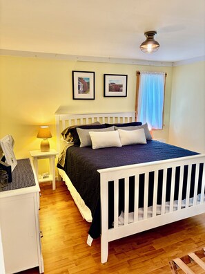 A bedroom with a white bed, a bedside table with a lamp, and two framed pictures on the wall. - Cozy Vermont Lake Lodge with Kayaks Fishing & Campfire Fun (Ryegate)