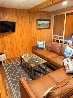A cozy room with wooden walls, a leather sofa, a television, and a framed landscape painting.