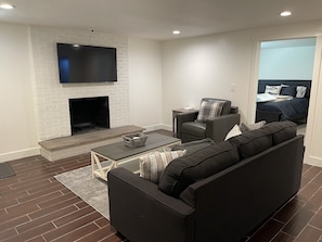 Una sala de estar moderna con chimenea, un televisor de pantalla plana montado encima, un sofá, una mesa de centro y una cama en la habitación contigua.