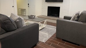 Una sala de estar moderna con chimenea, dos sofás grises, una mesa de centro y un televisor de pantalla plana montado en una pared de ladrillo.