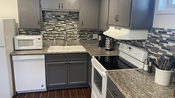Una cocina moderna con gabinetes grises, un microondas blanco, un lavamanos de acero inoxidable y un horno negro.