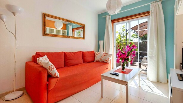 Un salon lumineux avec un canapé rouge, une table basse blanche et une grande fenêtre avec des rideaux.