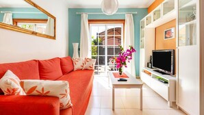 Un salon avec un canapé rouge, un téléviseur et une fenêtre avec des rideaux.