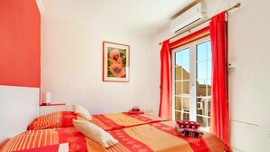 Une chambre à coucher avec un lit, une fenêtre avec des rideaux, un appareil de climatisation et un tableau encadré au mur.