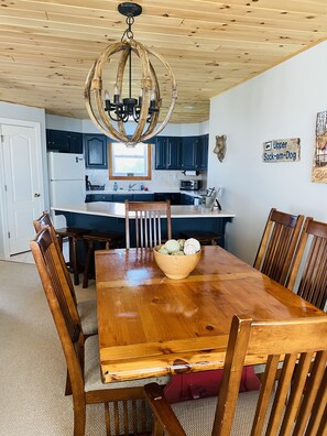 A wooden dining table with chairs, a chandelier, and a bowl of fruit.