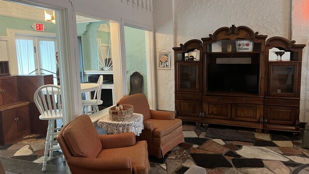 A living room with two brown armchairs, a small table with a basket, a wooden cabinet with a TV, and a patterned floor.