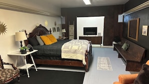 A bedroom with a bed, bedside table, lamp, chair, sofa, TV, and a small table with a plant.