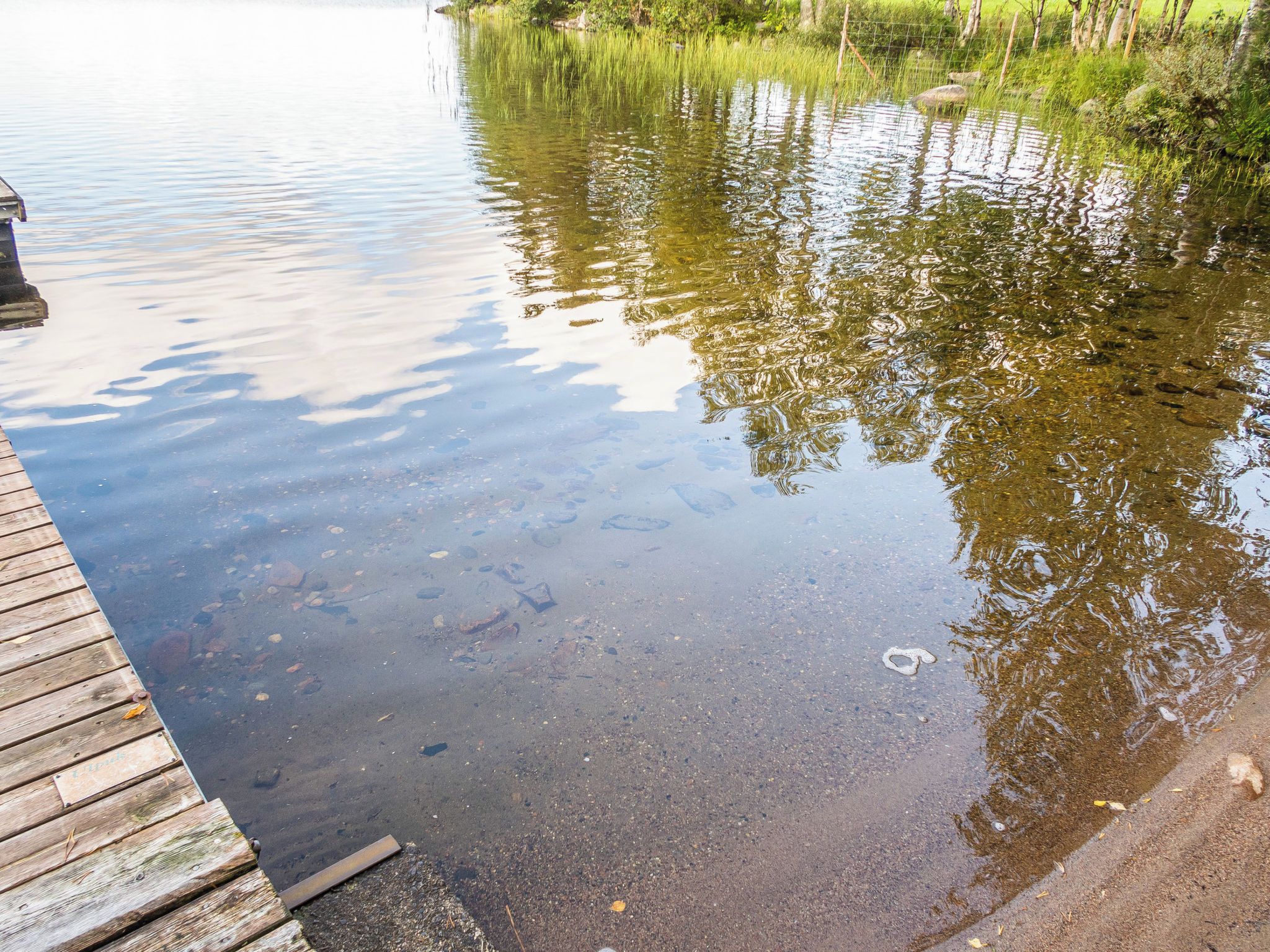 A wooden dock extending into a calm body of water with clear reflections of surrounding trees.