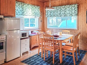 A compact kitchen with a refrigerator, microwave, and stove. There is a dining table with chairs and a window with curtains.