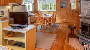 Un intérieur de chalet chaleureux avec des murs en bois, un coin repas, une cuisine équipée d’une cuisinière et un téléviseur.