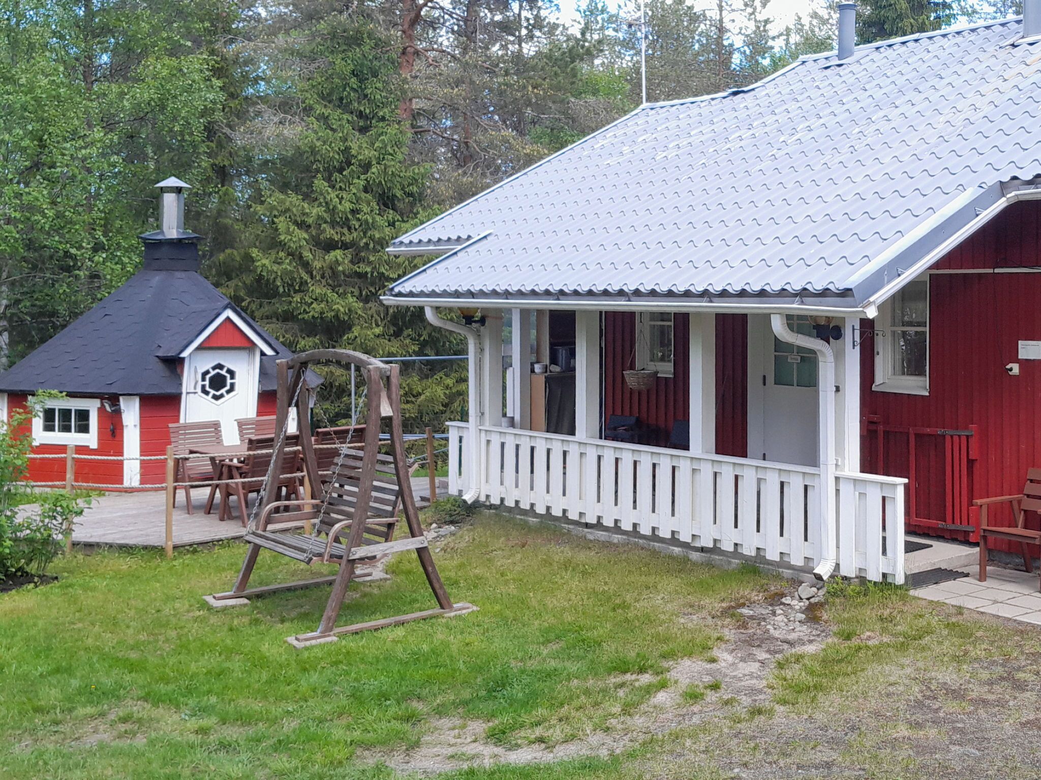 A red building with a white porch, a swing set, and a small red and white structure with a chimney.