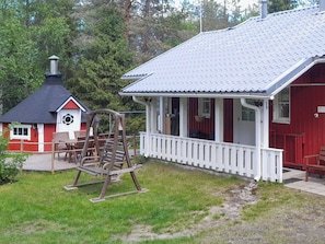 Un bâtiment rouge avec un porche blanc, une balançoire et une petite construction rouge et blanche dotée d’une cheminée.