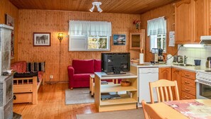 L’intérieur chaleureux d’un chalet avec un revêtement mural en bois, un canapé rouge, un téléviseur, un coin cuisine et une table à manger.