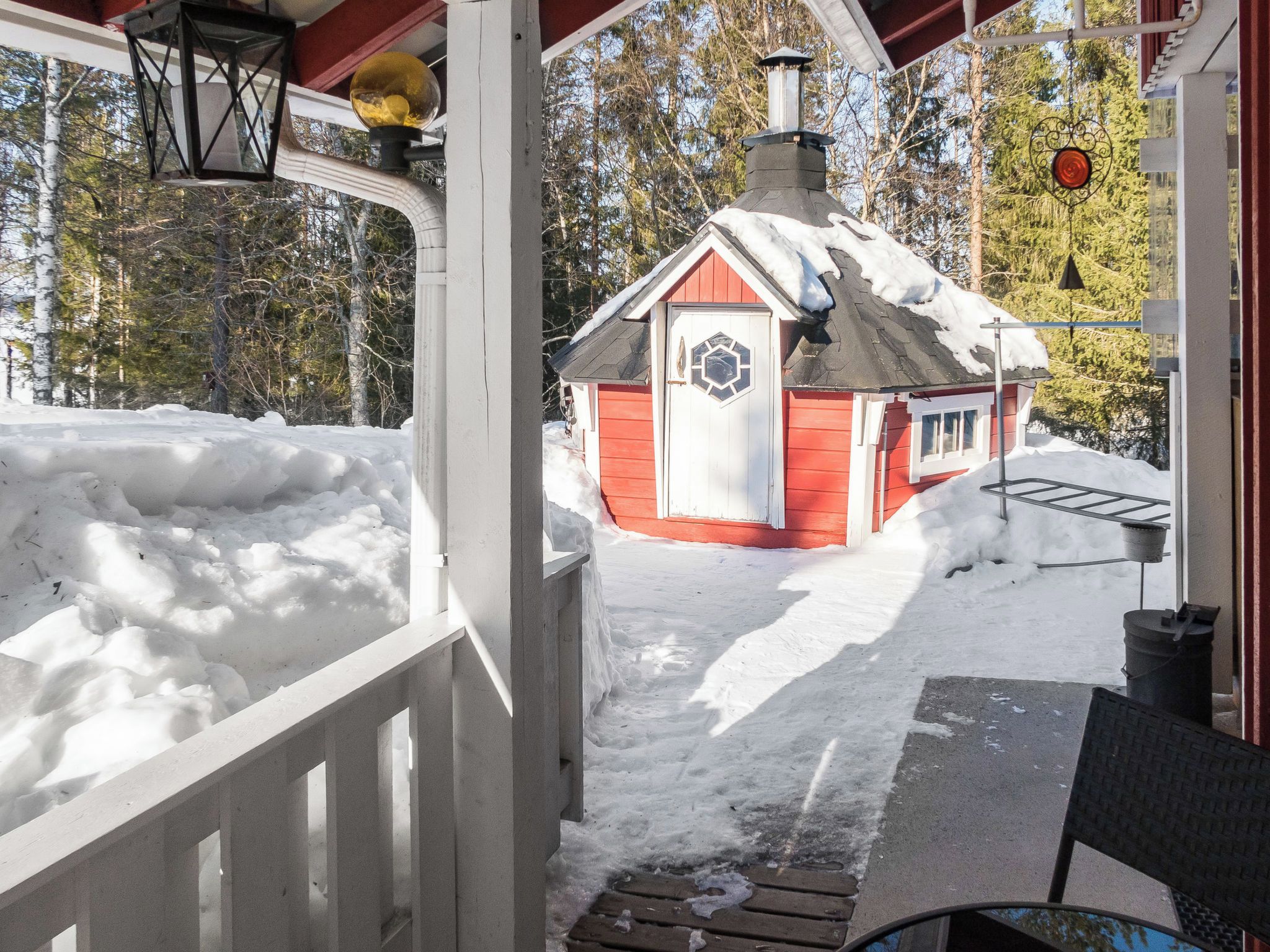 A covered porch with a red cabin in the background.