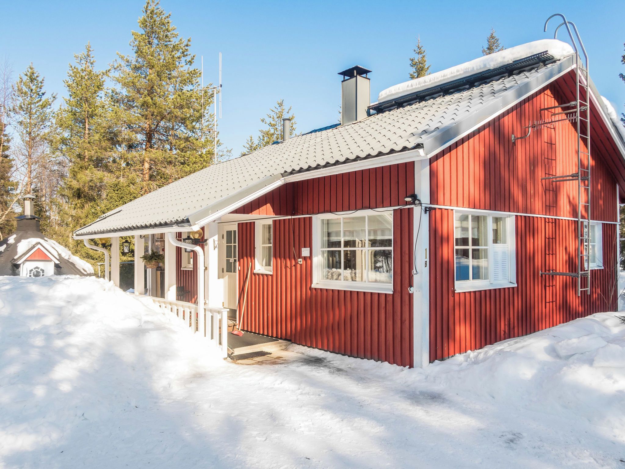 A red wooden cabin with a sloped roof, a chimney, and a small porch.