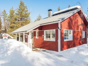 Une cabane en bois rouge, avec un toit en pente, une cheminée et un petit porche.