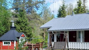 Une cabane rustique dotée d’une cheminée, d’une balançoire en bois et d’un coin repas avec une table et des chaises.