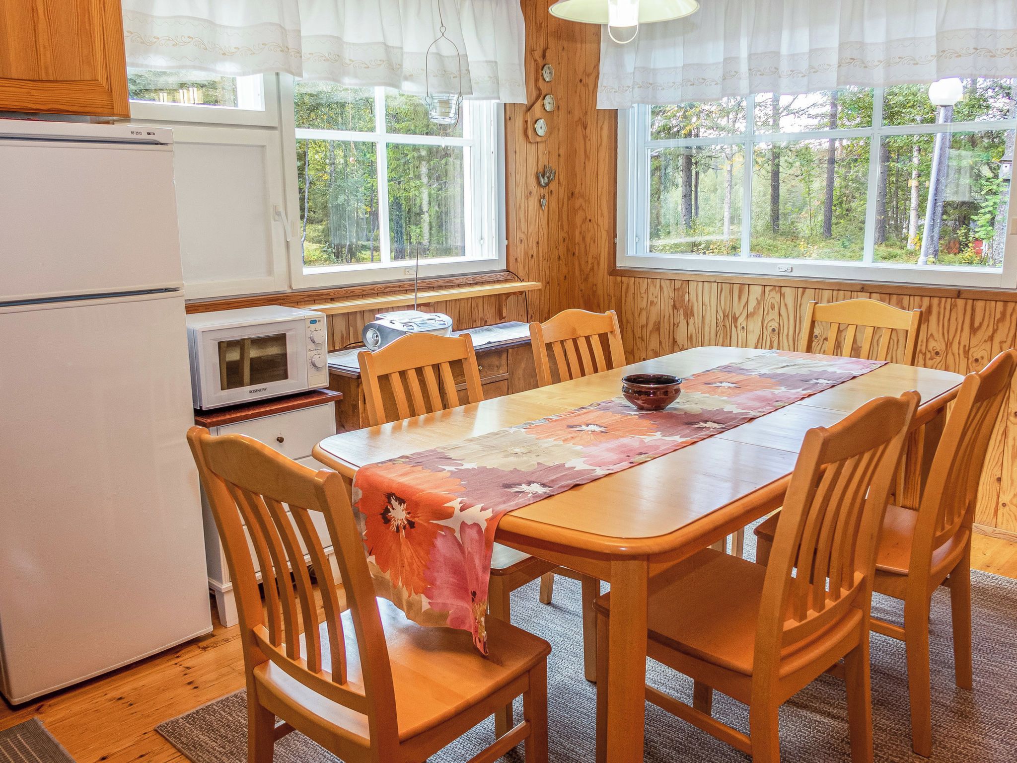 Eine kompakte Küche mit Holzausbau, einem Kühlschrank, einer Mikrowelle und einem Esstisch mit Stühlen.
