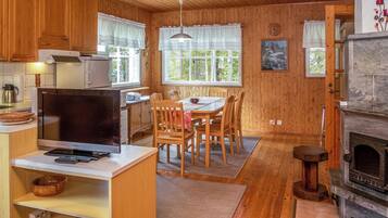 Un intérieur de chalet chaleureux avec des murs en bois, un coin repas avec une table et des chaises, une cuisine équipée et une cheminée.