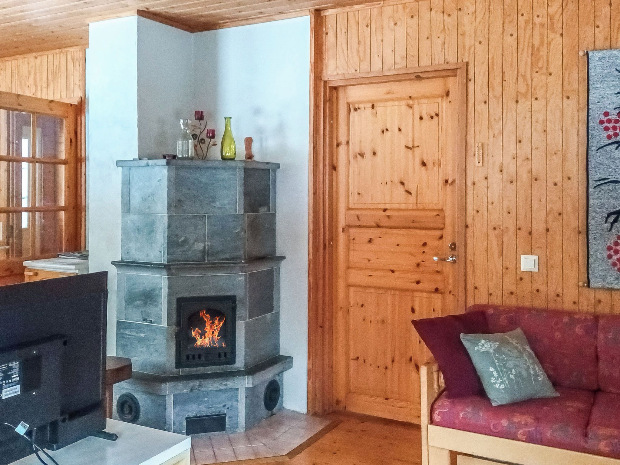 Ein gemütliches Zimmer mit Kamin aus Stein, Holzwänden, einem roten Sofa und einem Fernseher.