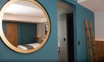 A bedroom with a circular mirror, a bed, a wooden door, and a ladder.