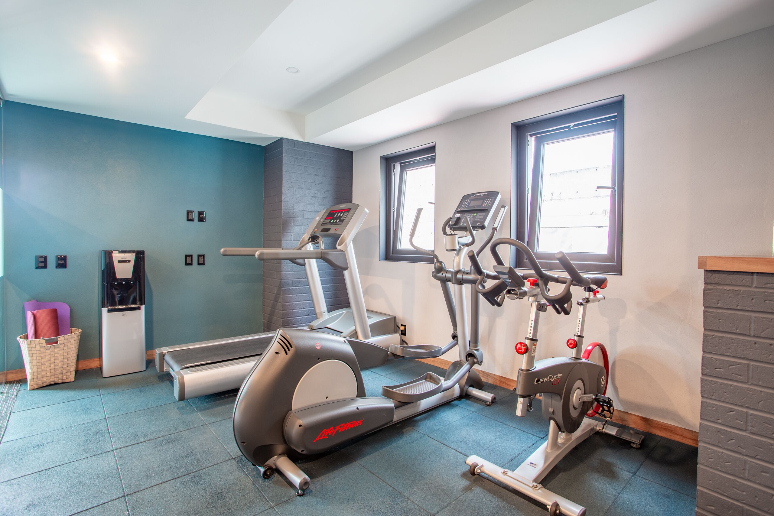A gym with cardio machines, a water dispenser, and a basket with mats.