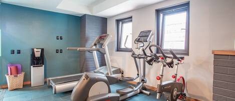 A gym with cardio machines, a water dispenser, and a basket with mats.