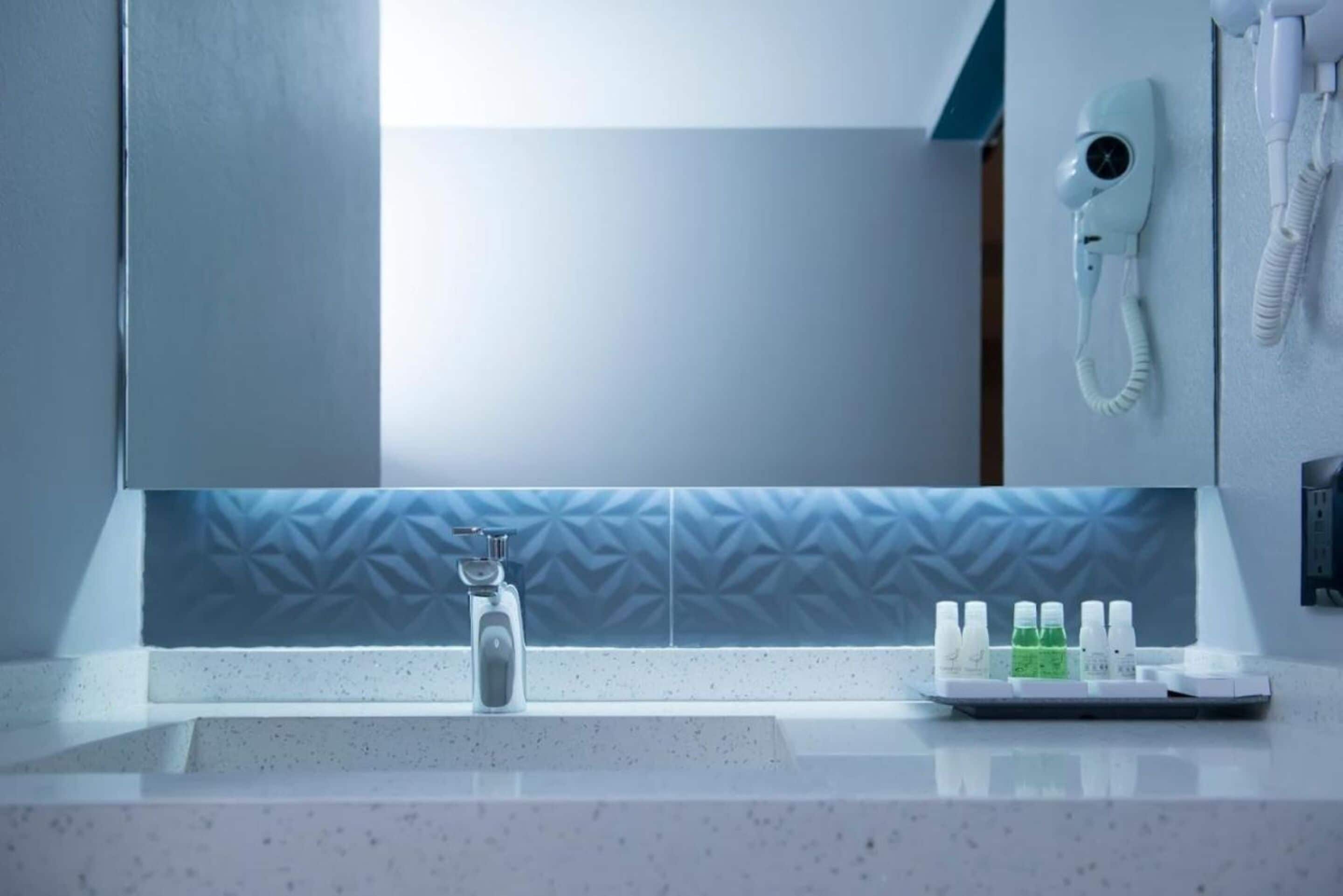 A bathroom with a sink, a mirror, a hairdryer, and a tray with toiletries.