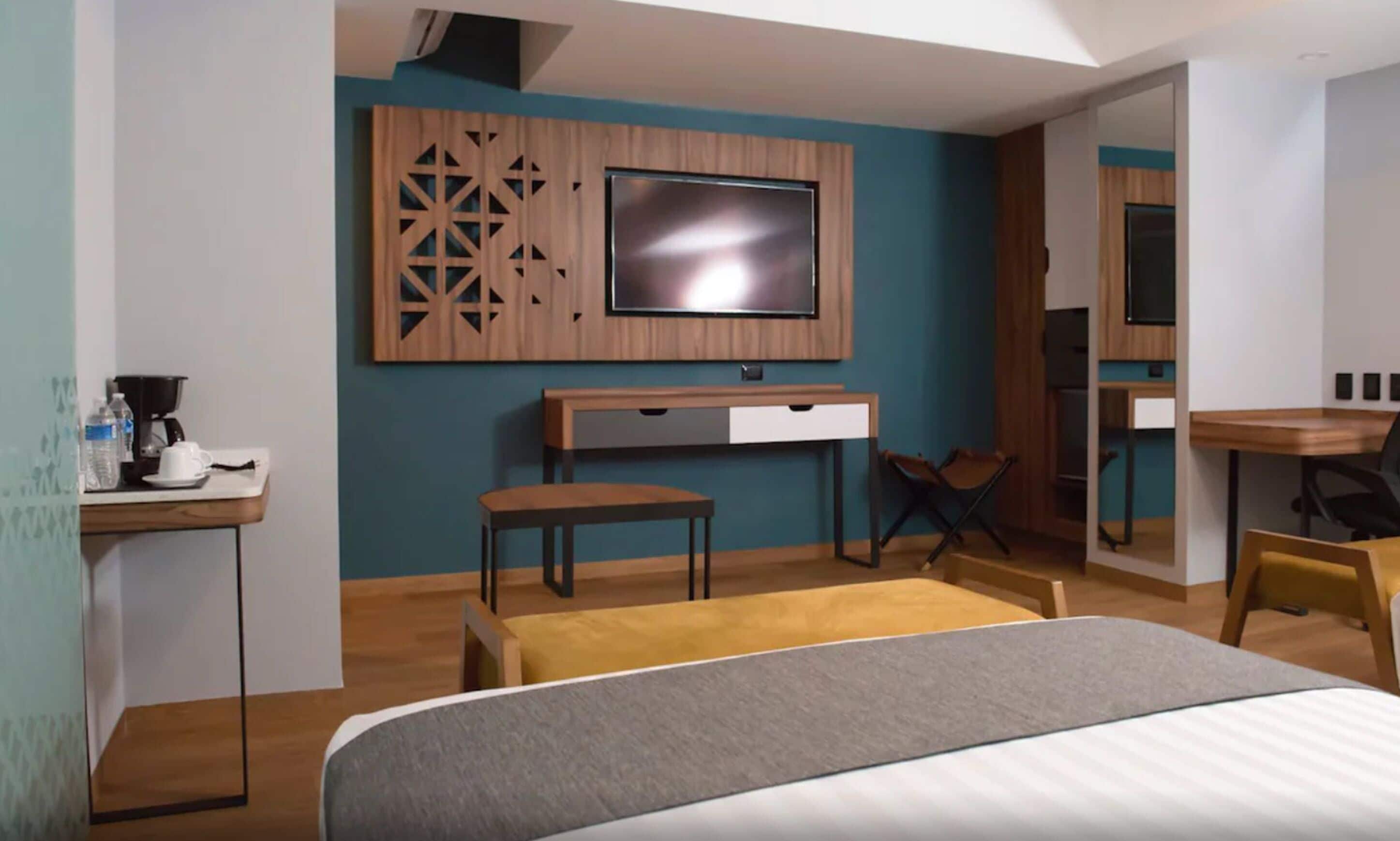 Une chambre d’hôtel moderne dotée d’un grand lit, d’un bureau avec un ordinateur, d’un téléviseur fixé au mur et d’un petit coin salon.