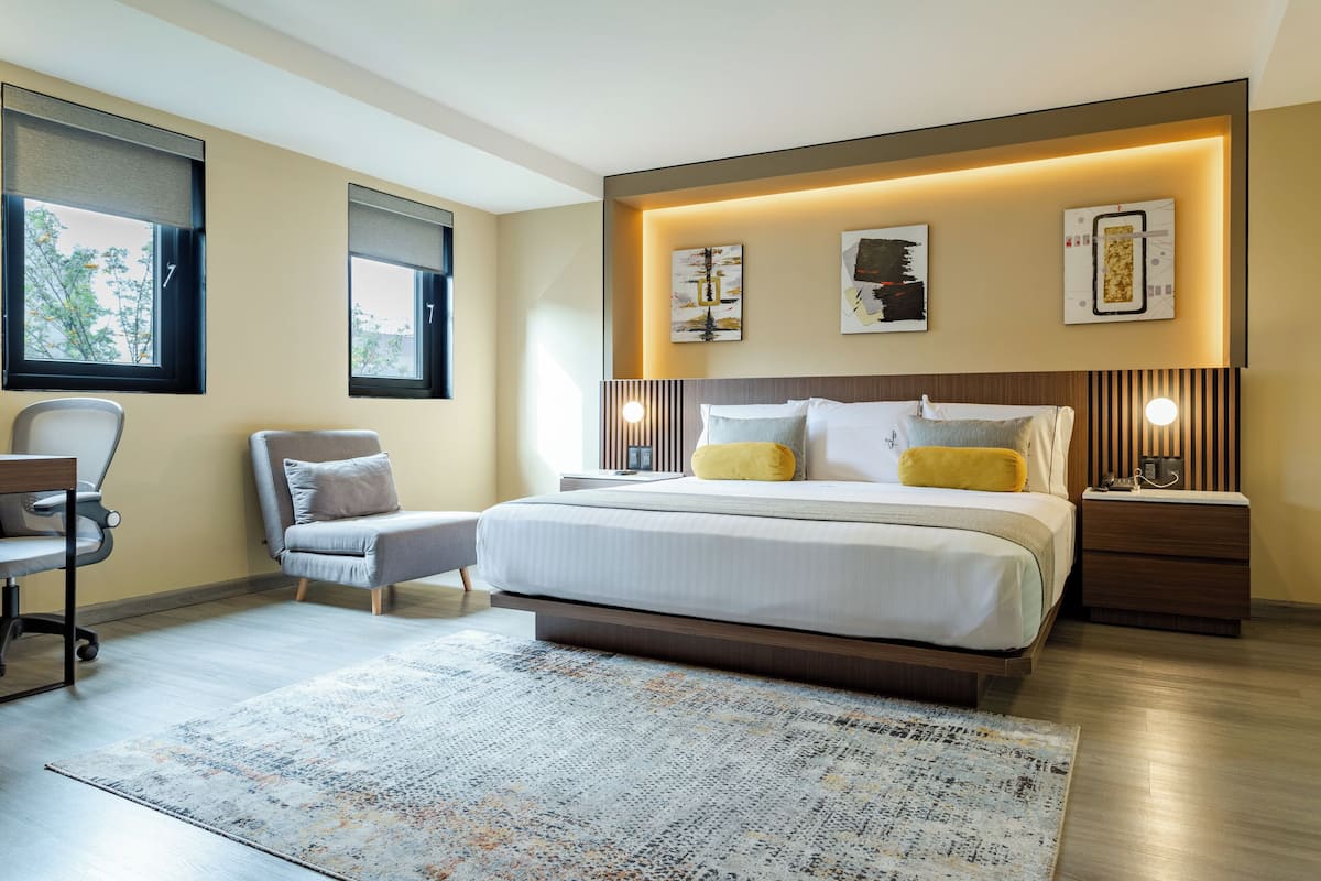 Un dormitorio moderno con una cama grande, mesitas de noche, una silla y obras de arte en las paredes.
